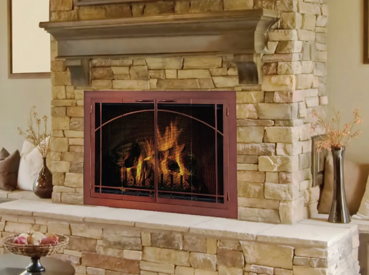 A Design Specialties arched glass door with a fire burning behind it, set into a stone fireplace