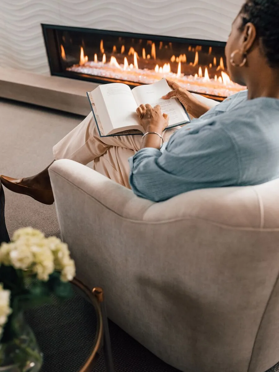 Reading in an armchair beside a linear gas fireplace in the evening